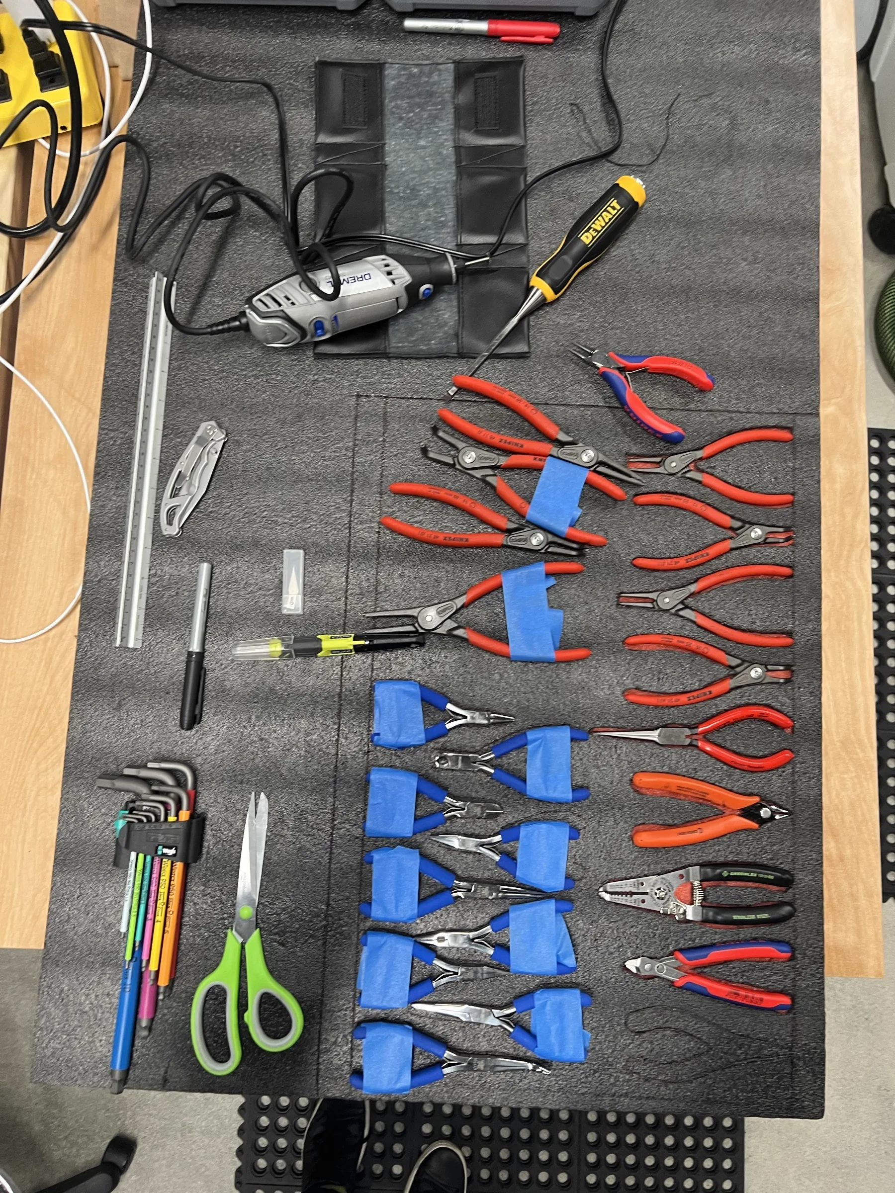 Pliers, scissors and a DeWalt rotary tool laid out on black foam with painter's tape templating, the day before the foam is cut