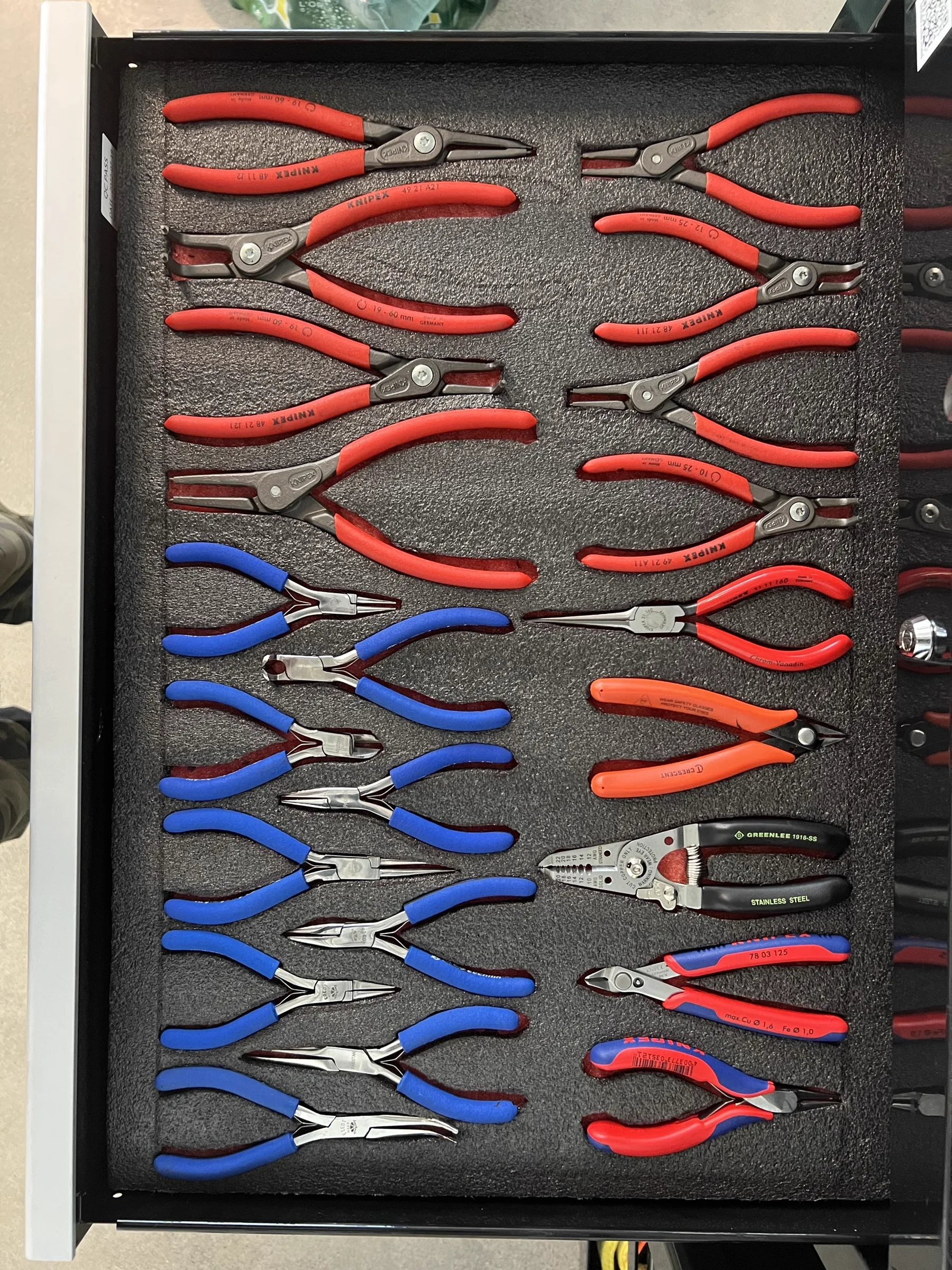 A drawer of red and blue handled precision pliers, arranged in rows on black foam